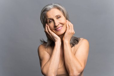 Gri üzerinde izole edilmiş kameraya bakan yaşlı, güzel, gri saçlı kadın.