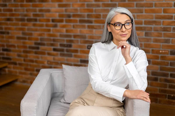 Retrato de una elegante y elegante mujer de negocios madura de mediana edad, ceo en gafas sentadas en la oficina moderna y posando con los brazos cruzados — Foto de Stock