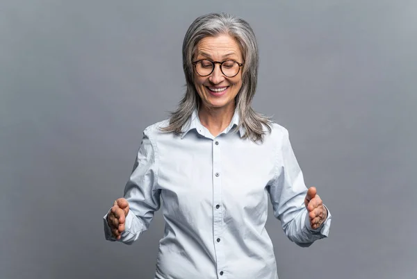 手の長さを示すシニア成熟した白髪の実業家は、灰色で隔離されたシンボルを測定します。眼鏡の女性マネージャー立っていると何か大きなもののサイズを実証 — ストック写真