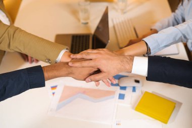 Ofisteki sabah toplantısında rahat atmosferde masada oturan genç çalışanlar. Ellerini birbirine bağlayan insanlar. Çok ırklı takım