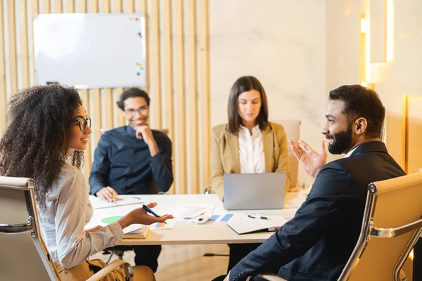 Discussion d'affaires au bureau contemporain de l'équipe multiraciale. Ils sont assis autour de la table et s'écoutent avec un sourire — Photo