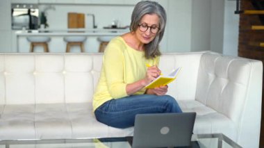 Odaklanmış emekli kadın çevrimiçi dersler için dizüstü bilgisayar kullanarak internetten öğreniyor.
