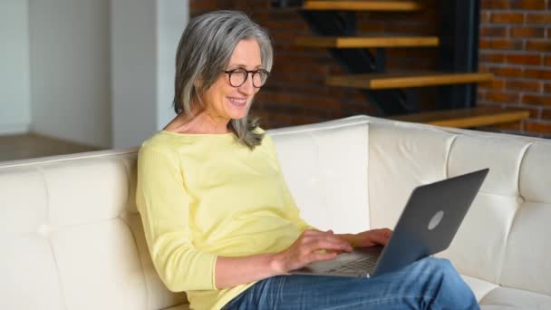 Evden video bağlantısı için dizüstü bilgisayar kullanan mutlu yaşlı kadın. — Stok video