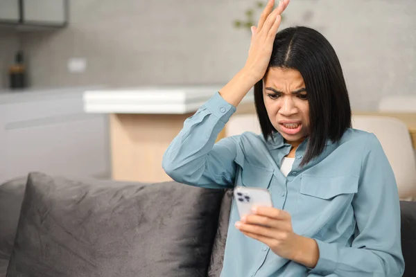 Confused young woman looking at smartphone screen, feeling depressed about bad news notification. Upset millennial female worrying about received spam scam message — Fotografia de Stock