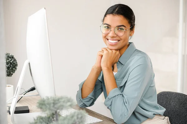 Belle et intelligente jeune fille multiraciale portant des lunettes élégantes à l'aide d'un ordinateur dans un appartement confortable. E-étude, travail à distance — Photo