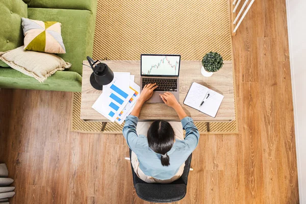 Masada oturan ve dizüstü bilgisayarda yazan melez etnik kadın ya da kadın serbest yazar genel bakış açısına göre not alıyor. Modern ev ofisi