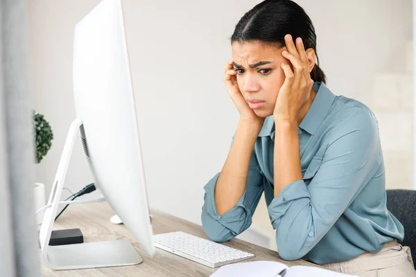 Bored female office employee sitting at the desk in front of computer, looking away and feeling sad. Pensive young woman does not have inspiration for work, feels lack of sleep — Fotografia de Stock