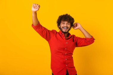 Heyecanlı, sakallı, şık kıyafetler giymiş, dans eden, elini kaldıran ve eğlenen, keyifli İspanyol bir adam. Kapalı stüdyo çekimleri turuncu renkte.