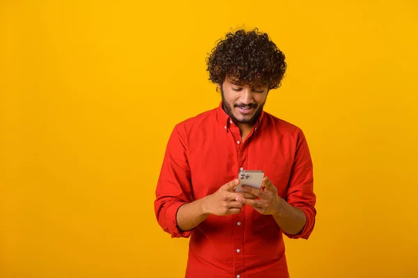 Pas up pohled na šťastný hezký blogger mladý dospělý muž stojící, pomocí smartphonu a textové zprávy s úsměvem. Vnitřní, izolované, studio shot, oranžové pozadí — Stock fotografie