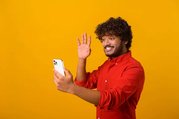 Positive bearded man smiling making selfie on smartphone camera, blogger communicating, recording video for followers in social networks. Indoor studio shot isolated — стоковое фото