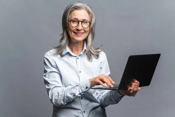 Portrait of the clm smiling woman holding laptop and looking at the camera with pleasure smile. Indoor studio shot isolated on grey — ストック写真