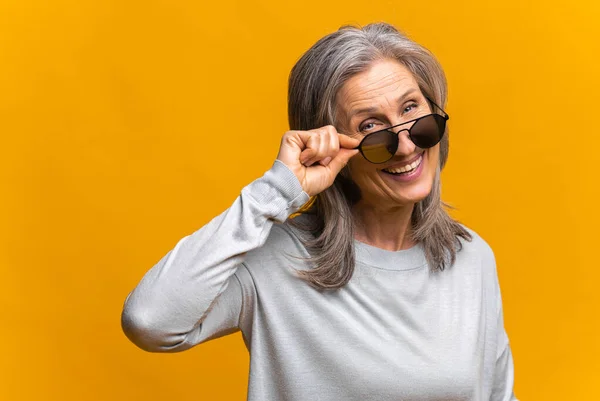Photo of confident mature female model wears trendy sunglasses, prepares for date, isolated on yellow background — ストック写真