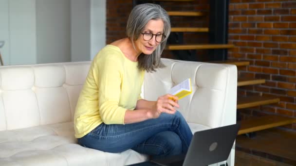 Concentrated mature gray-haired woman in glasses using laptop for online studying — Stock Video