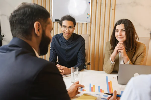 Ryhmä nuoria itsevarmoja liikemiehiä keskustelee jotain viettäessään aikaa toimistossa — kuvapankkivalokuva