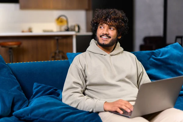 Cheerful Indian man wearing casual wear sitting on the sofa and using laptop — Stock Photo, Image
