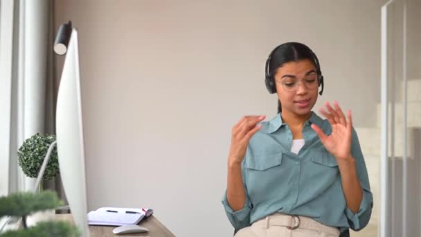 Θετική νεαρή γυναίκα που φοράει ακουστικά μιλώντας στο διαδίκτυο, χρησιμοποιώντας υπολογιστή για σύνδεση βίντεο — Αρχείο Βίντεο