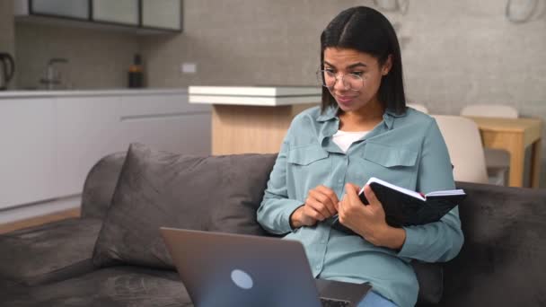 Smiling mixed-race teenage girl female student sitting on the couch with laptop — Wideo stockowe