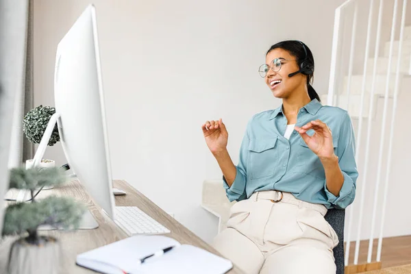 Позитивна молода жінка в гарнітурі розмовляє онлайн, використовуючи ноутбук для відеозв'язку з колегами або клієнтами, весела жінка-працівник працює віддалено — стокове фото