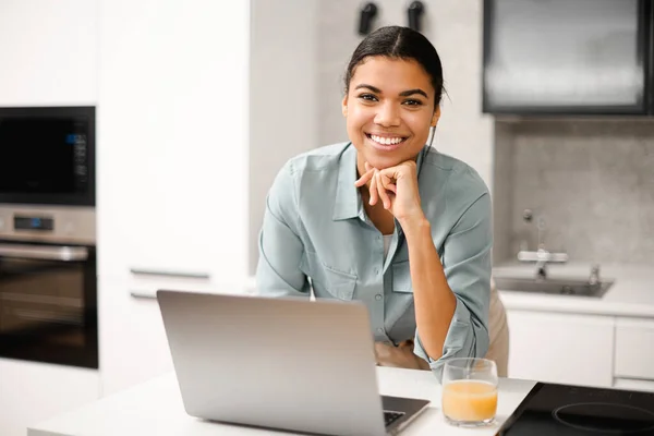 Весела молода жінка використовує ноутбук для віддаленої роботи в домашньому офісі. Усміхнена бізнес-леді змішаної раси в повсякденному вбранні тримає відеодзвінок, вводячи електронну пошту — стокове фото