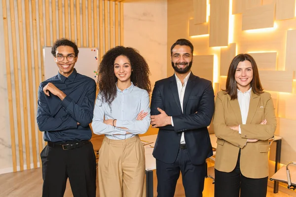 Cohesive cheerful team of young professionals standing in office wearing smart casual clothes. Informal atmosphere in multiracial team, cosy office — Fotografia de Stock