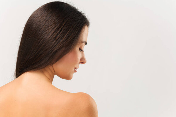 Back view of attractive asian woman, looking down and smiling, skincare concept