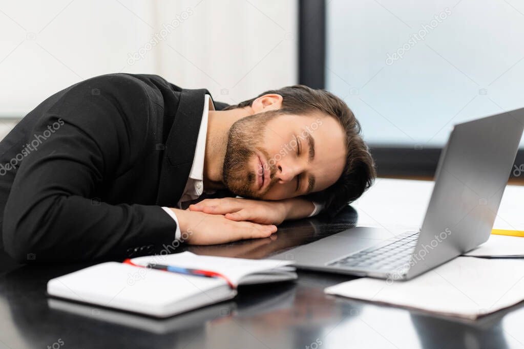 Tired young businessman in formal wear taking a nap on the workplace