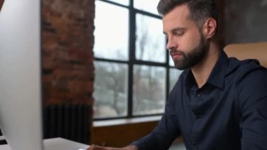 Depressed young male office employee is staring at computer monitor with despair