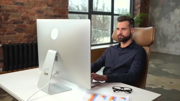 Εστιασμένος και χαμογελαστός άντρας με έξυπνο casual πουκάμισο κοιτάζοντας την οθόνη του φορητού υπολογιστή — Αρχείο Βίντεο
