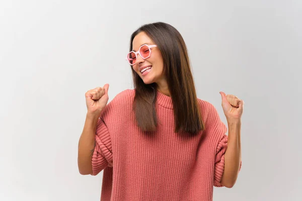 Excited enthusiastic woman in sunglasses dancing isolated on white. Crazy overjoyed female in pink jumper raising hands up, moving in beats — Foto de Stock