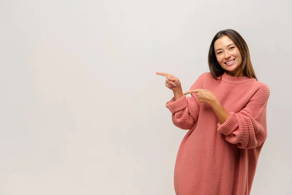 Asian woman pointing aside with fingers, having happy facial expression. Indoor studio shot isolated — Stock Photo, Image