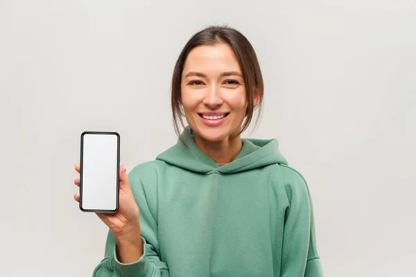 Positive optimistic woman holding out smartphone with blank screen for advertisement or promotion — Stock fotografie