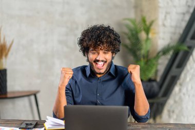 Excited Pakistani businessman looking at the laptop screen and rejoicing. Guy screaming yes staring with mouth opened at monitor amused with unexpected opportunity