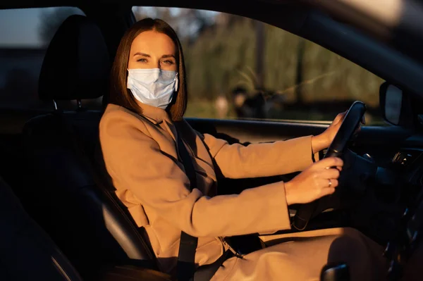 Молода жінка в розумній випадковості в захисній медичній масці за кермом автомобіля — стокове фото