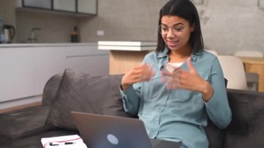 Kanepede otururken bilgisayar başında video görüşmesi yapan çok kültürlü bir kadın.