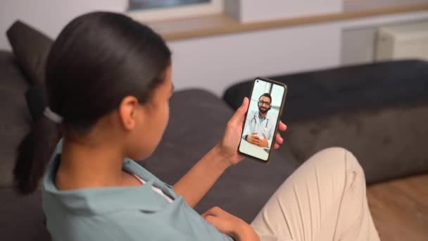 医者とのビデオ通話のためのスマートフォンを使用して正の若い女性 — ストック動画