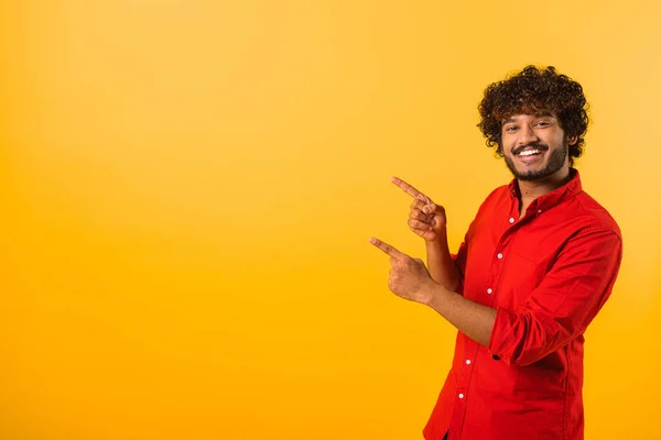 Agréable regardant l'homme bouclé pointant du doigt vers l'espace de copie, montrant la zone pour la publicité. Studio intérieur tourné isolé sur orange — Photo