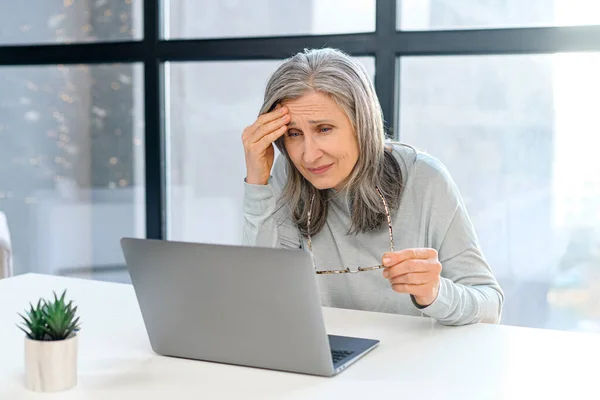 Concentré bouleversé femme âgée assise au bureau en face du PC profondément dans les pensées — Photo
