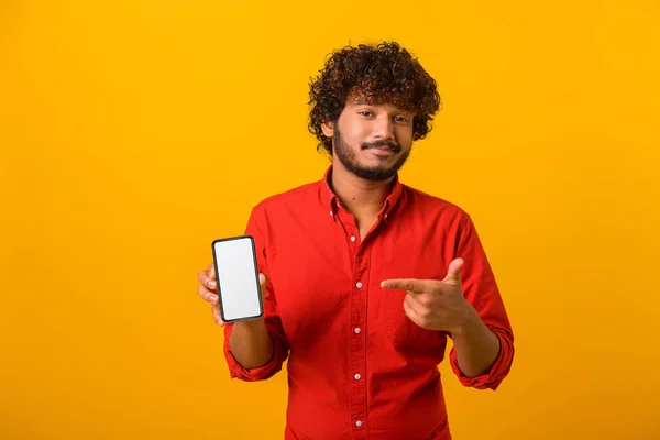 Skeptický muž ukazuje na displej chytrého telefonu a mračí se, ukazuje hrozné aplikace, zklamaný v online nabídce, stojící nad oranžovým pozadím — Stock fotografie