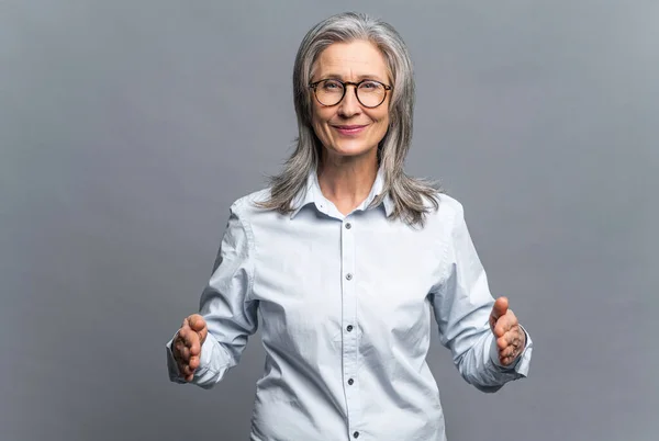 Mira esta gran cosa. Senior madura mujer de negocios de pelo gris mostrando un gran objeto con las manos en el espacio vacío. Anciana en gafas de pie y demostrando el tamaño de algo grande — Foto de Stock