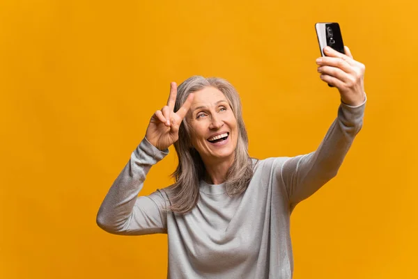 スマートフォンで自撮りをしたり、ビデオ通話や笑顔で話したり、モバイル通信をしたりする陽気な女性の肖像。屋内撮影、黄色の背景 — ストック写真