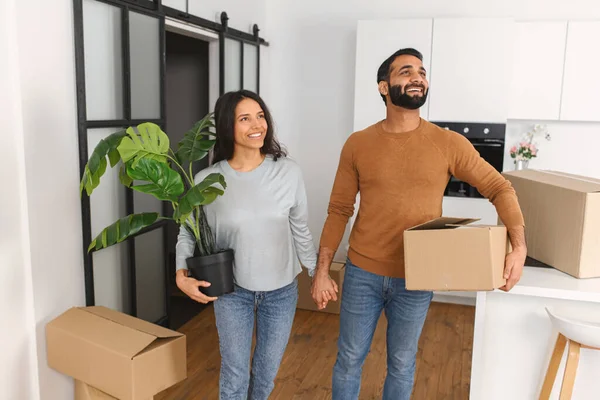 Gelukkig stel vraagt zich af met neef nieuw huis na de verhuizing. Een gelukkige man met kartonnen doos en een band met een vrouw die planten vasthoudt. Onroerend goed huur, hypotheek en eigendom — Stockfoto