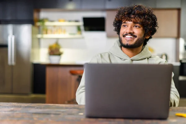행복하고 낙관적 인 인도 남자, 현대 아파트에서 노트북을 사용하여 평상복 차림. 성공적 인 영감을 받은 아랍 남성 사업가는 시선을 돌리고 사려 깊게 웃습니다 — 스톡 사진