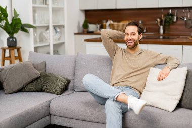 Genç beyaz adamın portresi kanepede dinleniyor, geleceği düşünüyor. Eli kafasında yakışıklı, olumlu bir adam oturma odasında oturuyor ve dinleniyor.