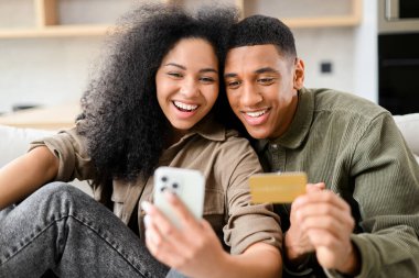 İnternetten alışveriş yapan çok neşeli bir çift. Heyecanlı çok ırklı kadın ve elinde akıllı telefon ve kredi kartı olan adam. Çevrimiçi alışverişler, sipariş verme