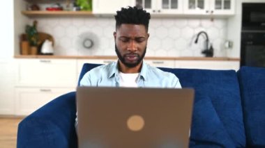 Evdeki kanepede oturan ve dizüstü bilgisayar kullanan talihsiz bir Afro-Amerikalı.