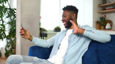 Heyecanlı, dişlek gülümsemeli, video bağlantısı için akıllı telefon kullanan Afro-Amerikalı adam.
