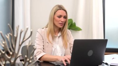 Dizüstü bilgisayarın önünde aktif bir iş kadını. İnternette çalışıyor ya da çalışıyor. Yazıyor.