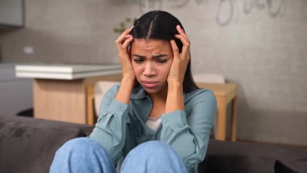 Mujer afroamericana triste sentada en el sofá y llorando desesperada — Vídeo de stock