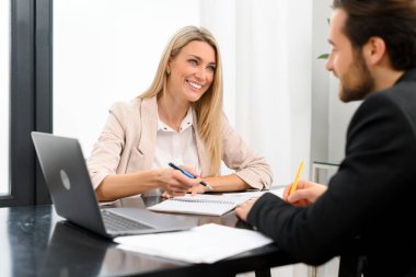 Ofisteki bankacılar. Ofiste dizüstü bilgisayarla çalışan beyaz gömlekli bir adamın portresi. Gömlekli kız yakınlarda oturuyor.