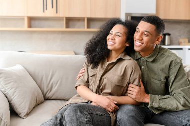 Mutlu, çok ırklı, birbirine aşık bir çift kanepede oturup sarılıyor ve başka tarafa bakıyor. Gülümseyen adam ve kız arkadaşı sarılıyor. Aşk ve sevgi